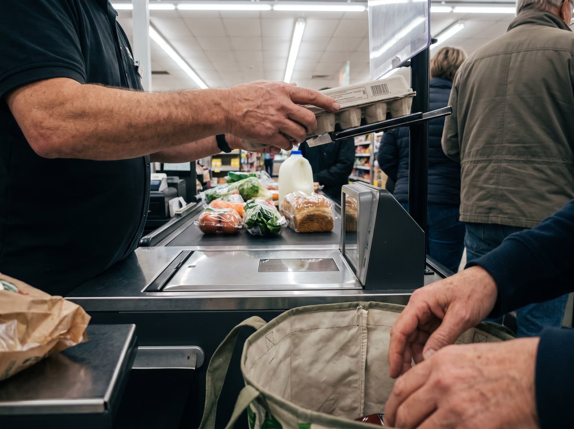 A cashier sliding eggs across a flatbed scanner at a grocery checkout lane