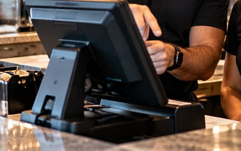 A trainer’s hand guiding staff through the POS screen at the counter
